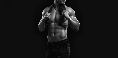 Obraz premium Muscular model sports young man on dark background. Black and white fashion portrait of strong brutal guy. Sexy torso. Male flexing his muscles. Sport workout bodybuilding concept.