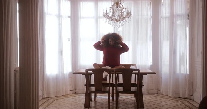 Black woman on dining room table dancing gesturing with arms