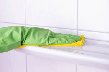 cleaning lady in the bathroom washes a shelf in green gloves