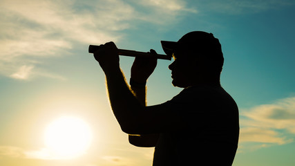 A silhouette of a man looking at using a monocular telescope against a dramatic sky at sunset....