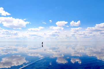 Fototapeta na wymiar Silhouette walking on the calm water of the lake Elton, the biggest salt lake in Europe, with amazing mirror reflections of sky and clouds, Russia, Volgograd oblast