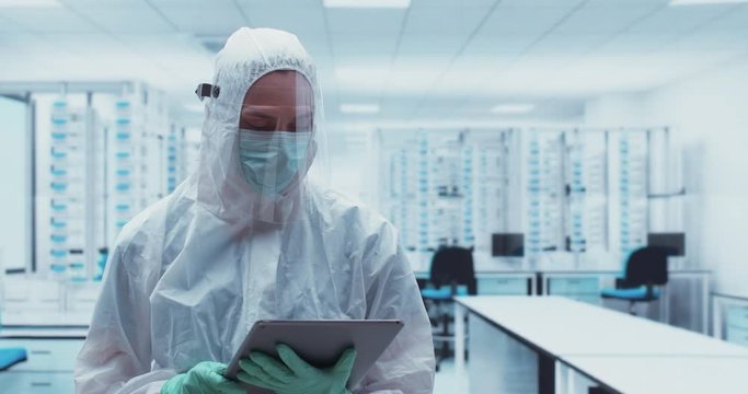 Caucasian female wearing protective hazmat suit and face shield using tablet in a laboratory