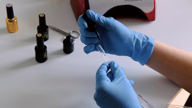 Manicurist's hands are coloring artificial fake nails sample template with shellac UV gel and putting them into a UV lamp nail hardener.
Fingernail treatment, salon care, polishing. Female manicure"