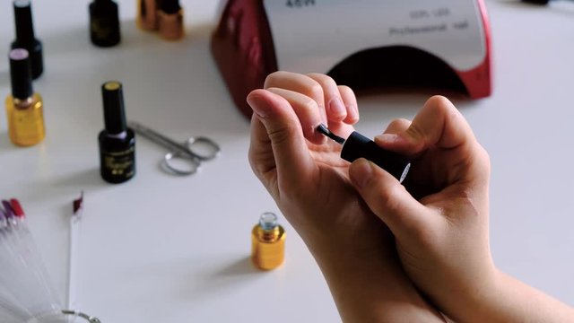 The woman putting UV gel base on her nails. the woman is covering her nails with the nail polish. Fingernail treatment, salon care, polishing and grinding, Female manicure in the light environment.