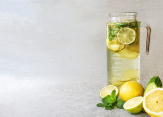 Homemade lemonade made from lemon, lime and cucumber in a tall glass carafe, with fruit and vegetables in the bottom. Grey background, close-up, horizontal, copy space