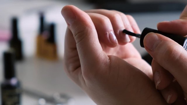 Close up of the woman's hand applying UV gel base on her nails. the woman is covering her nails with the nail polish UV gel base. Female manicure in the light environment.