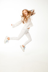 A girl with long hair, dressed in white colored clothes, is jumping on a white background.