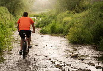 boy with orange shirt during a cycling adventure along a creek. Flare and light effect, scenic...