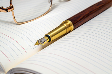 Gilt pen and glasses rests on an open notebook for notes or writing text