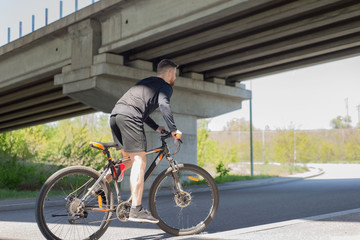 athlete, bearded guy cyclist, rides on the highway on a sports bike. Under the bridge. Outdoors. Spring sports.