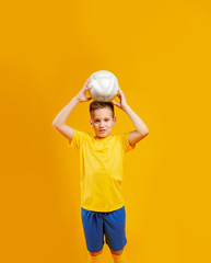 boy plays soccer ball in studio on a yellow background