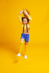 cute cheerleader girl in a yellow tank and blue shorts holds pompons and dances / jumps