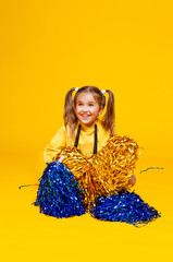 cute cheerleader girl in a yellow tank and blue shorts holds pompons