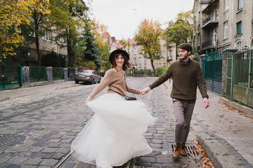 Naklejka premium Romantic and happy caucasian couple in casual wedding clothes walking and hugging at the city streets. Love, relationships, romance, happiness, urban concept. Man and woman celebrate their marriage.