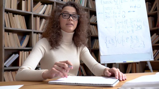 Female young hispanic school math teacher, college tutor coach looks at camera in classroom speaking virtual teaching remote class, online lesson, elearning video conference zoom call. Webcam view.