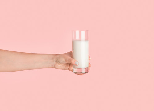 Girl hand showing glass full of milk on pink background, closeup