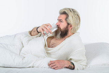 Man drink water in bed. Bearded man in bathrobe. Morning routine. Morning and wake up. Everyday life. Overworked man.
