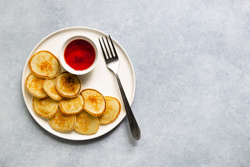 Trendy pancake cereal meal. Tiny baked pancakes with berry jam on white plate.. Breakfast food at home. Table top view, flat lay