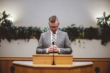 Male in a grey suit preaching words of the Holy Bible at the altar of a church