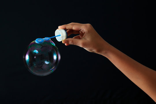 Rainbow Soap Bubble With Hand Holding Bubble Wand Isolated On Black