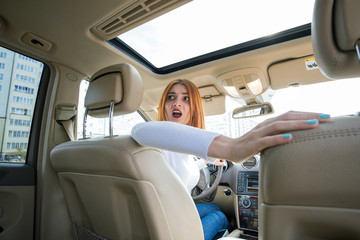 Wide angle view of young redhead woman driver driving a car backwards looking behind.