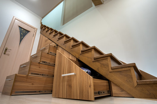 Modern architecture interior with luxury hallway with glossy wooden stairs in multi-storey house. Custom built pullout cabinets on glides in slots under stairs. Use of space for storage.
