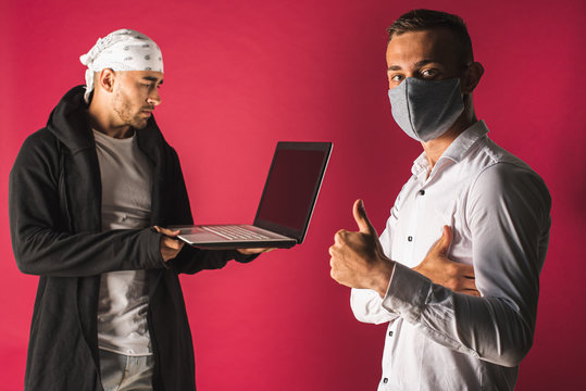 Portrait Of Two Young People, One Working On Computer The Other In Medical Protective Mask Isolated On Red Background. Sociability, Pandemic, Protection