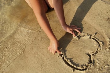 girl's hands draw a heart on a sand