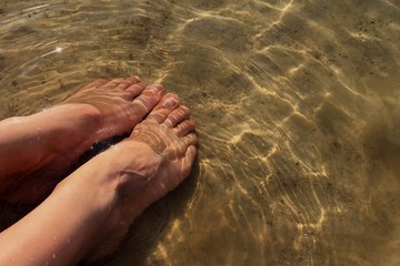 female feet on sand in water 