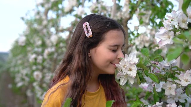Portrait of teenage girl smelling white apple tree flowers