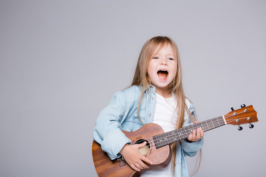 The girl sings and plays the ukulele. The child laughs, poses for the camera and enjoys the music. Learning to play ukuleles
