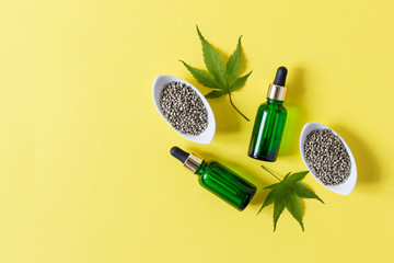 Glass bottles with CBD oil, dry and fresh hemp leaves, hemp seeds on yellow background top view.