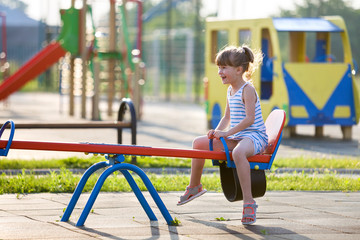 Fototapeta na wymiar Cute young child girl outdoors on see-saw swing on sunny summer day.