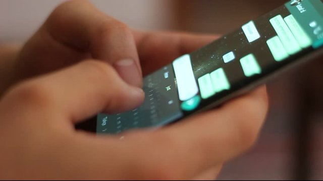 Young man using smartphone while doing homework. Young people and college education. Male student studying and texting with mobile telephone at home, typing text message on cell phone. Close-up