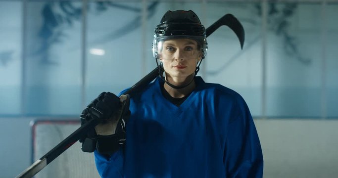 Portrait shot of happy beautiful young Caucasian female hockey player in helmet and with club smiling cheerfully on ice arena. Joyful pretty sportswoman with stick.
