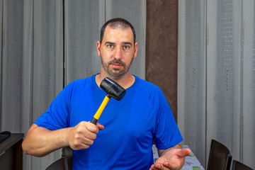 Man with a beard and short hair in a blue shirt with a rubber hammer in a defiant attitude