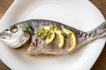 Dorada fish fried with lemon and parsley on a white plate