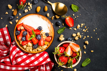 Greek yogurt granola with fresh berries on black stone table.