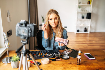 Beauty blogging. Young attractive girl makes makeup and recording video tutorial on the camera....