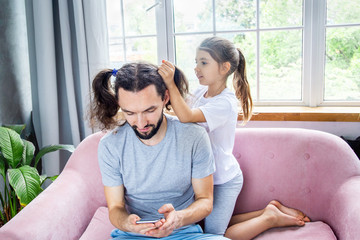 Father's day concept. Cute little girl doing a cheerful hairstyle to her father. Happy childhood and great relationships. Father and daughter spending time together. Happy family staying at home.