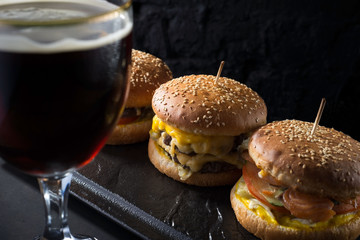 close-up, beer glasses with craft dark and light beer with foam, against a background of burgers, with a variety of ingredients, including shyomga, beef meat patty, cheese burger. In a rustic style