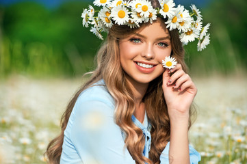 Beautiful young girl with curly hair in chamomile field.  Beautiful girl with chamomile wreath and blue dress on flowering field in summer. Beautiful curly hair. Freedom concept.