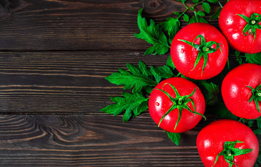 Fresh large tomatoes with leaves on the right side of the frame are located on a dark vintage wooden background. Ripe tomatoes in droplets of water. Copy space for text, flat lay