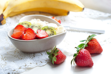 Breakfast with oatmeal with strawberries, kiwi and bananas on white background. Breakfast for child. Oatmeal in a white heart-shaped plate. 