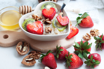 Breakfast with oatmeal with strawberries, kiwi, honey, walnuts and egg on white background. Breakfast for child. Oatmeal in a white heart-shaped plate. 