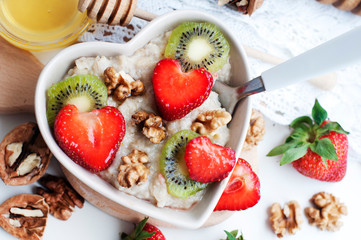 Breakfast with oatmeal with strawberries, kiwi, honey, walnuts and egg on white background. Breakfast for child. Oatmeal in a white heart-shaped plate. Top view