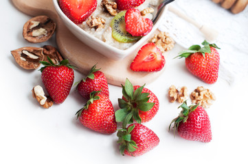 Breakfast with oatmeal with strawberries, kiwi, honey, walnuts and egg on white background. Breakfast for child. Oatmeal in a white heart-shaped plate. Top view