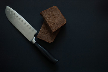 A steel knife with a black handle and two slices of brown bread lie on a black background. Healthy eating