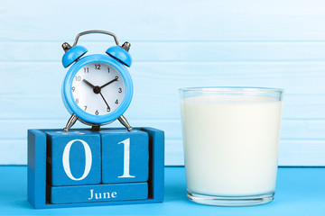 wooden calendar with the date of June 1, alarm clock and a glass of milk on a wooden background, World Milk Day