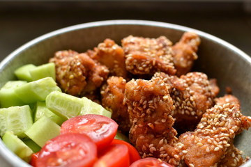 Tasty lunch in a gray bowl on a concrete background. Nuggets with sesame seeds. Cucumbers and tomatoes. Salad and chicken. Close up